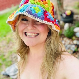 May include: A colorful, handmade crochet bucket hat. The hat features a vibrant patchwork design with squares of red, orange, yellow, green, blue, and purple. The brim is trimmed with a white crochet border. A cheerful and stylish accessory.