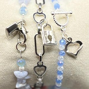 May include: Three silver bracelets with blue and white beads. The bracelets feature heart and padlock charms.