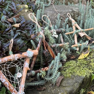 May include: Three triangular ornaments crafted from natural twigs and branches, bound with green twine. One features a woven white web with a small circular bead, another holds a dark crystal, and the third is adorned with a small feather.