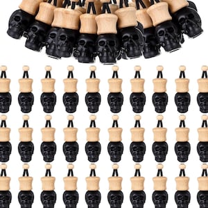 May include: A collection of black skull-shaped car air fresheners with wooden tops and black cords. The skulls are detailed and the wooden tops are light brown. The air fresheners are arranged in rows against a white background.