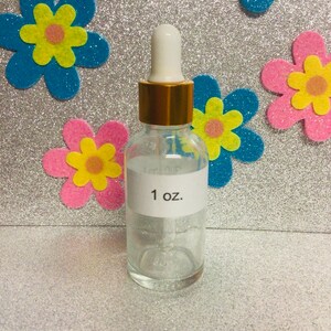 May include: A clear glass bottle with a gold lid and a white dropper. The bottle is labeled "1 oz."