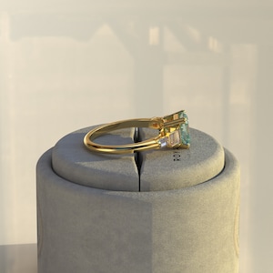 May include: A gold ring with a large, emerald-cut aquamarine gemstone and smaller baguette-cut diamonds. The ring is displayed on a gray ring box with the word "ROYAL" printed on it.