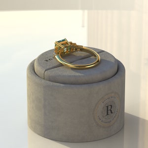 May include: A gold ring with a large emerald-cut green gemstone surrounded by smaller diamonds. The ring is displayed on a gray ring box with the text "Royal Blue Lab Diamond Jewelry" printed on the side.