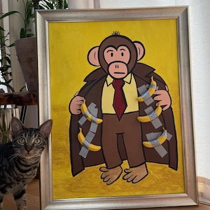 Pode incluir: Pintura emoldurada de um macaco usando um casaco marrom, terno e gravata vermelha, com bananas presas ao casaco. O fundo é amarelo. Uma moldura prateada envolve a obra de arte. Um gato tigrado está em primeiro plano.