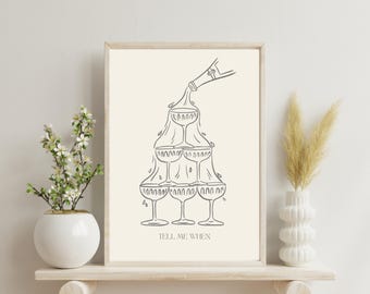 May include: A framed print featuring a champagne tower illustration in black ink on a cream background. The image shows champagne pouring into a pyramid of glasses. The text "TELL ME WHEN" is at the bottom. The print is displayed on a wooden shelf.