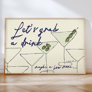 May include: A framed print with a minimalist design of martini glasses and olives. The navy blue text reads "Let's grab a drink" and "maybe a few more...". The artwork has a light cream background. The print is in a wooden frame.