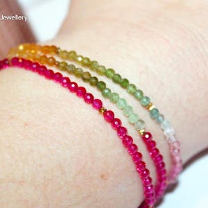 May include: Three delicate beaded bracelets in shades of pink, green, and yellow-orange. The bracelets are made of small, round beads and gold accents. The bracelets are worn on a wrist.