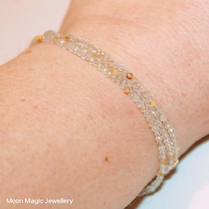 Könnte beinhalten: Ein zartes Armband aus mehreren Reihen winziger, klarer und goldener Perlen. Das Armband wird am Handgelenk getragen.