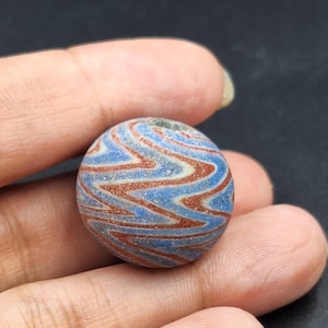 May include: A round glass bead with a swirling pattern of blue and red. The bead has a hole in the center for stringing.