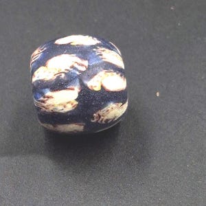 Könnte beinhalten: Eine blaue Glasperle mit weißen und gelben Mustern. Die Perle ist rund und hat eine glatte Oberfläche.