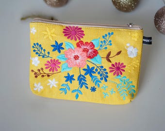 May include: Yellow zippered pouch with a floral embroidery design. The embroidery features pink, blue, white, and red flowers. The pouch has a label that says "MADE IN"