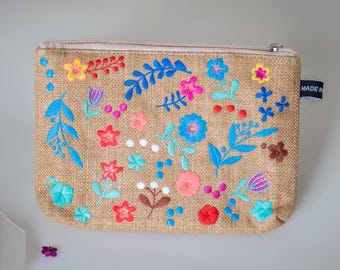 May include: A beige burlap cosmetic bag with a zipper closure and a colorful floral embroidery design. The embroidery features blue, pink, red, yellow, and white flowers and leaves.