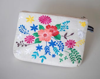 May include: A white zippered pouch with a floral embroidery design. The embroidery features pink, red, blue, yellow, and green flowers and leaves.