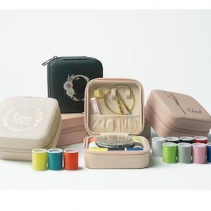 Puede incluir: Un conjunto de seis pequeñas cajas de costura cuadradas de color beige con diferentes diseños. Las cajas tienen una tapa con bisagras y están llenas de carretes de hilo. Las cajas están dispuestas en una fila sobre una superficie blanca.