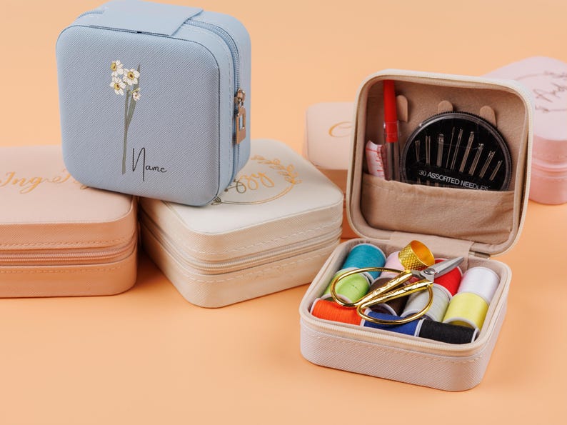 K&ouml;nnte beinhalten: Vier verschiedene quadratische Etuis mit Rei&szlig;verschluss. Ein Etui ist hellblau mit einem Blumenmuster und dem Text "Name". Ein weiteres Etui ist cremefarben mit einem Blumenmuster und dem Text "Good Vibes". Ein drittes Etui ist hellrosa mit dem Text "Inspire". Das vierte Etui ist cremefarben mit einem Rei&szlig;verschlussfach, das eine Vielzahl von N&auml;hzubeh&ouml;r enth&auml;lt, darunter Nadeln, Garn und eine Schere.