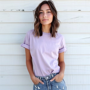 May include: A woman wearing a light purple t-shirt with rolled up sleeves and blue denim jeans.