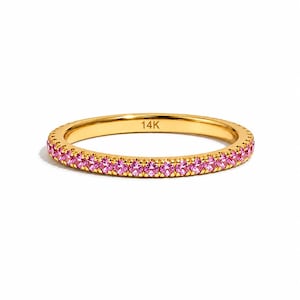 Könnte beinhalten: Ein dünner Goldring mit einer durchgehenden Reihe kleiner, runder, leuchtend rosa Edelsteine, die auf der Außenseite gefasst sind. Auf der Innenseite des Rings ist deutlich der Schriftzug 14K eingeprägt, der den Goldgehalt des Schmuckstücks angibt.