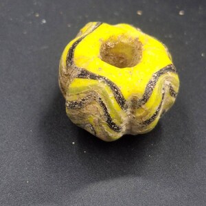 May include: A yellow glass bead with black stripes. The bead has a hole in the center and is shaped like a star.