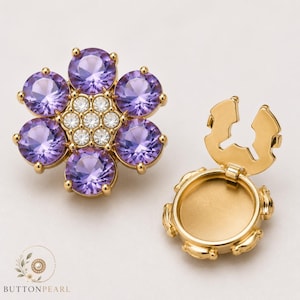Peut inclure: Un bouton en métal doré avec un dessus en forme de fleur orné de cinq grands cristaux violets ronds et sept cristaux transparents plus petits au centre. À côté se trouve un dos de bouton en métal doré ouvert avec une base circulaire creuse.