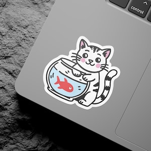 Pode incluir: Um gato branco e cinza com bochechas cor-de-rosa segura um aquário azul com um peixe dourado vermelho dentro. O gato está sorrindo e tem uma cauda listrada.