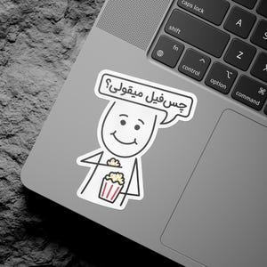 Könnte beinhalten: Ein Aufkleber mit einer Cartoonfigur, die Popcorn in einem rot-weiß gestreiften Behälter hält. Die Figur hat eine Sprechblase mit Text in einer Fremdsprache. Der Aufkleber befindet sich auf einem Laptop.