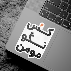 Könnte beinhalten: Ein weißer Aufkleber mit schwarzem arabischem Text, der "Kesh Neshoon" auf einem silbernen Laptop lautet.