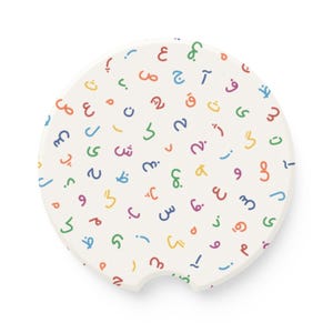 May include: A white ceramic car coaster with a colorful pattern of Arabic script letters and numbers. The design features a variety of colors, including red, orange, yellow, green, blue, and purple. The coaster has a small notch for easy removal.