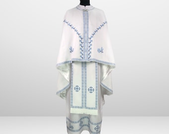 May include: White liturgical vestment with blue embroidered floral designs. The vestment features a long robe with a matching cape and a sash.