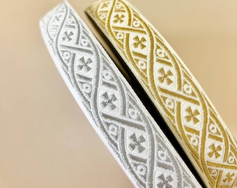 Pode incluir: Dois rolos de guarnição decorativa com fundo branco e um padrão repetido de cruzes prateadas e douradas.