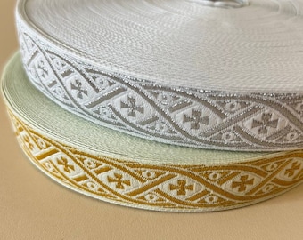 Pode incluir: Duas bobinas de fita decorativa. Uma é branca com um padrão geométrico prateado. A outra é verde-claro com um padrão geométrico dourado. As fitas estão enroladas, mostrando o design detalhado da borda.