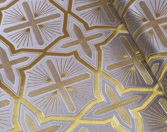 May include: A white fabric with a gold geometric pattern of repeating crosses and sunbursts. The fabric has a subtle sheen.