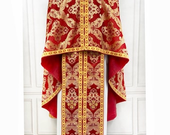 May include: A red and gold liturgical vestment with intricate patterns. The vestment has a long, flowing robe with a shorter, cape-like piece on top. The fabric is richly embroidered with gold thread.