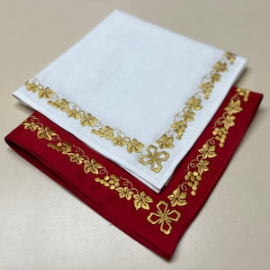 May include: Two embroidered napkins, one white and one red, with a gold vine and grape design around the border.