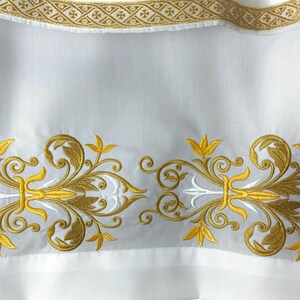 May include: White fabric with gold and white embroidery. The embroidery features a repeating pattern of stylized leaves and swirls.