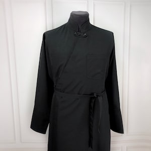 May include: Black wrap-style robe with a mandarin collar and long sleeves. The robe features a single pocket on the right side and a matching belt to cinch the waist. The fabric appears to be a lightweight material.