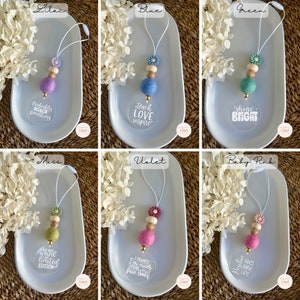 May include: Six different colour felt ball car charms with a clear acrylic charm with a saying on it. The colours are lilac, blue, green, moss, violet, and baby pink. The sayings are "Probably just something", "Teach Love Inspire", "Shine Bright", "I am world limited edition", "I promise I'm nicer than my face looks", and "Positive vibes make life better".