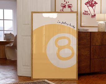 May include: A framed print with a yellow background and a white number eight in the center. The text "i'm feeling lucky" is written in cursive above the number. The print is hanging on a wall with two other framed prints above it.