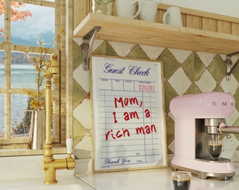 Puede incluir: Una máquina de espresso rosa con un vaso de espresso sobre una encimera blanca. Un cheque de huésped con el mensaje escrito a mano "Mamá, soy un hombre rico" está colgado en la pared detrás de la máquina de espresso.