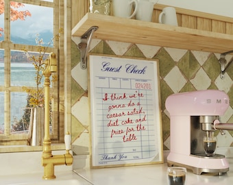 Puede incluir: Una máquina de espresso rosa con un vaso de café delante. Un cheque de invitado escrito a mano está en la pared detrás de la máquina con el texto "Creo que vamos a pedir una ensalada César, coca-cola light y patatas fritas para la mesa. Gracias."