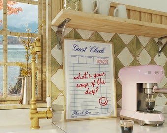 Puede incluir: Una máquina de espresso rosa con un vaso de café delante. Un cheque de invitado con el texto "what's your soup of the day?" está colgado en la pared detrás de la máquina.