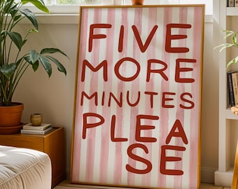 May include: A framed artwork with the text "FIVE MORE MINUTES PLEASE" in red letters on a pink and white striped background. The artwork is displayed in a bright room with plants and a window.