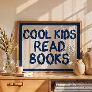 May include: A wooden framed print with the text "COOL KIDS READ BOOKS" in navy blue. The print is displayed on a wooden cabinet with decorative vases, a glass vase with wheat, and books. The scene is bathed in warm sunlight.