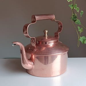 May include: A copper kettle with a hammered finish and a curved handle. The kettle has a spout and a lid with a knob.