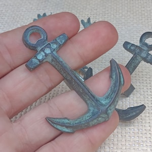 以下が含まれることがあります： 緑青の付いたアンティーク調の小さな金属製の錨が3つ。錨は、横木と2つの爪を持つ伝統的な船の錨の形をしています。