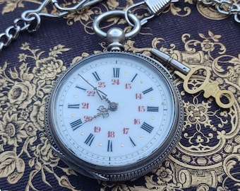 May include: A silver pocket watch with a white face and black Roman numeral hour markers. The watch has a key attached to it and is lying on a patterned fabric.