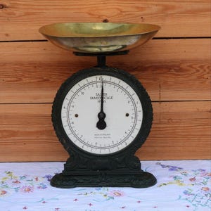 Könnte beinhalten: Eine schwarze Gusseisen-Küchenwaage Salter Family Scale No. 45 mit weißem Zifferblatt und schwarzen Markierungen. Die Waage hat eine große Schale aus poliertem Messing. Das Zifferblatt zeigt Messwerte in Pfund und Kilogramm an.