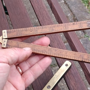 May include: A vintage wooden folding ruler with brass hinges and markings. The ruler is open, showing measurements in inches. The wood has a warm, aged tone, and the markings are clear and legible. A small brass piece is also visible.