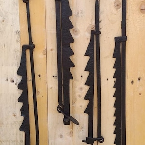 Pode incluir: Quatro ganchos de lareira em ferro forjado preto, cada um com uma barra vertical longa com uma série de dentes serrilhados para ajuste de altura e um anel circular no topo para pendurar, apresentando um acabamento metálico escuro e texturizado.
