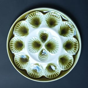 Puede incluir: Un plato de ostras de cerámica blanca con 12 hendiduras en forma de concha verde. El plato es perfecto para servir ostras u otros aperitivos pequeños.