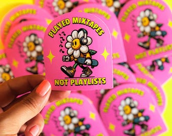 Puede incluir: Pegatina rosa con una flor de dibujos animados con auriculares y un monopatín. El texto en la pegatina dice "PLAYED MIXTAPES NOT PLAYLISTS". También se incluyen estrellas amarillas y notas musicales.